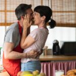 mature couple kiss in the kitchen sharing pineapple. concept of mature couple cooking