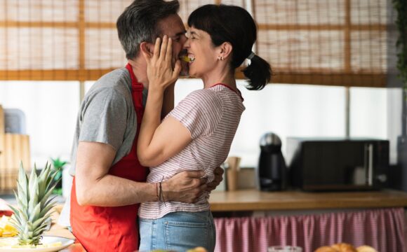 mature couple kiss in the kitchen sharing pineapple. concept of mature couple cooking