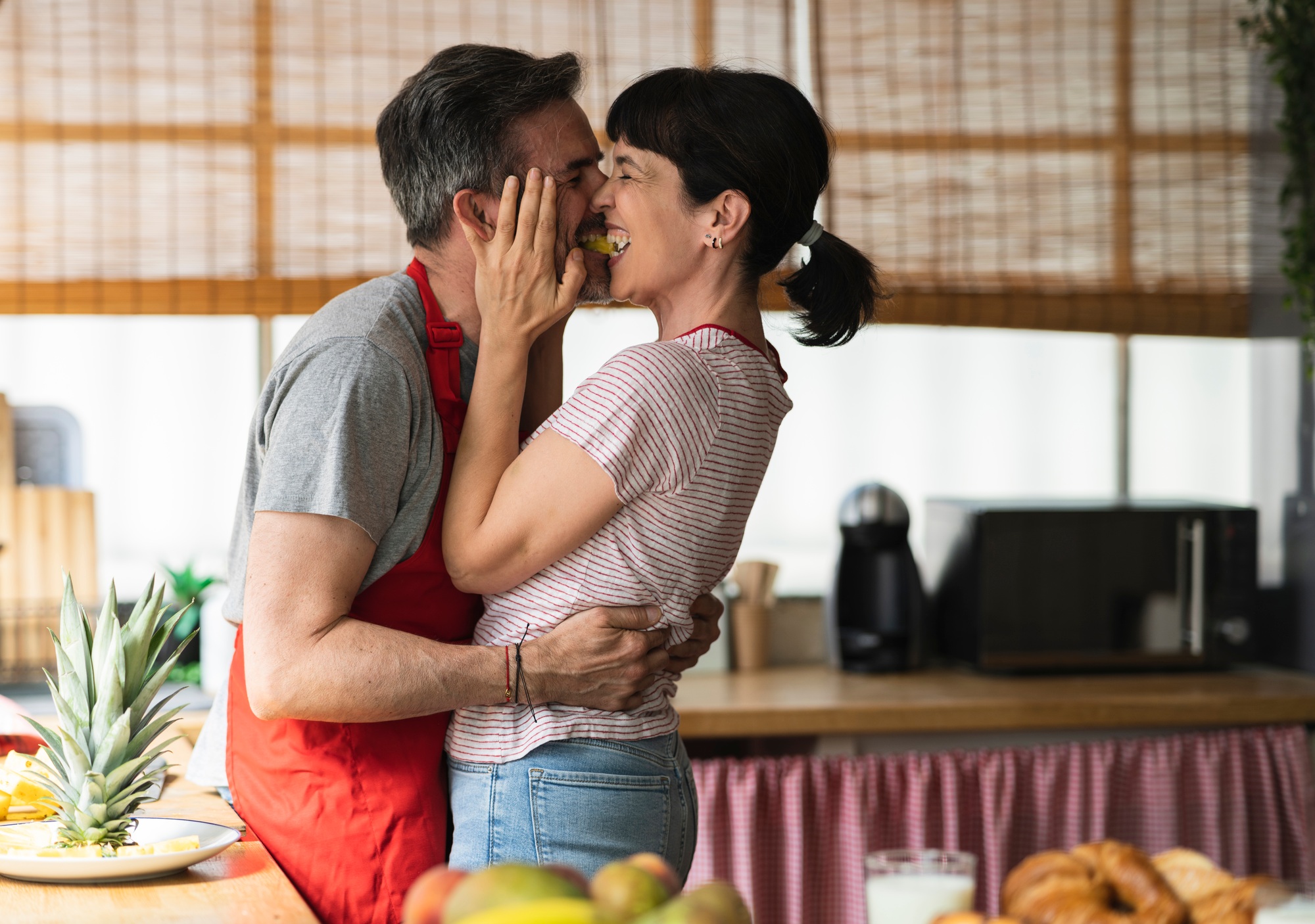 mature couple kiss in the kitchen sharing pineapple. concept of mature couple cooking